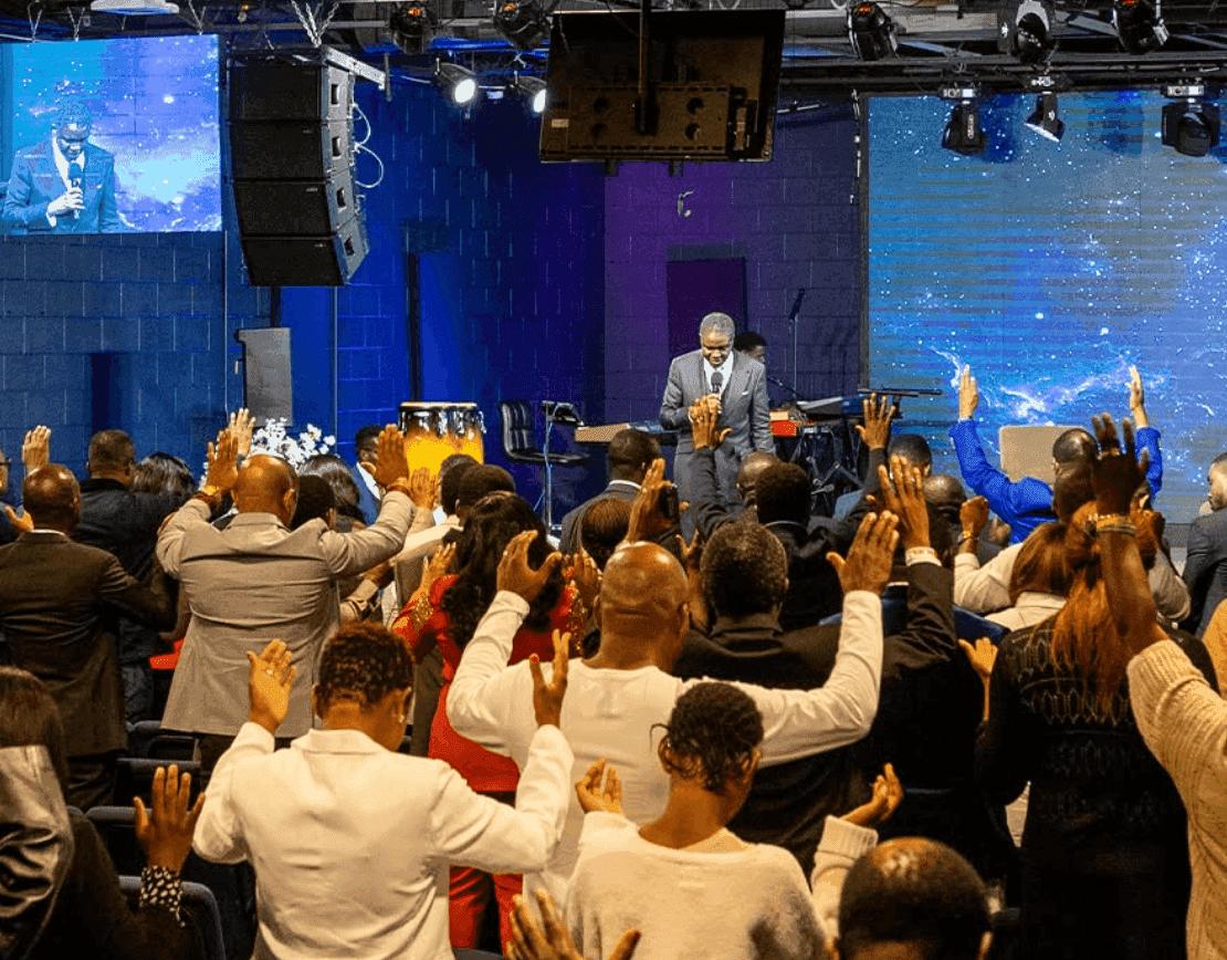 The entire congregation with hands raised in worship, blue stage lighting illuminating the moment