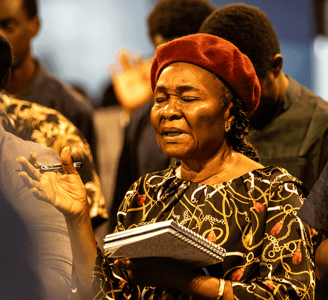 A woman minister with eyes closed in prayer, clutching her notebook