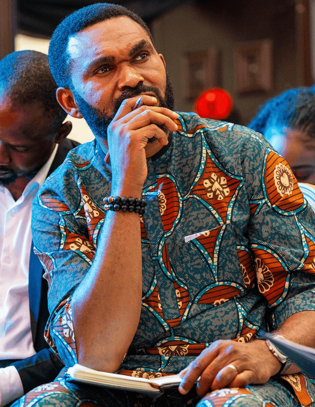 A young minister in African print attire, hand on chin, deep in thought during the conference